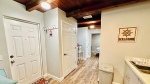 Un couloir avec des portes blanches, un panneau «Interdiction de fumer», un panneau d’accueil et un coin cuisine équipé d’un évier et de placards.