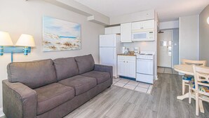 Een ruimtelijk ingerichte leefruimte met een bank, een eettafel met stoelen, een kitchenette met een magnetron en een koelkast.