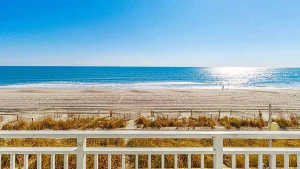 Een strand met een witte omheining op de voorgrond, een heldere blauwe lucht en de oceaan op de achtergrond.