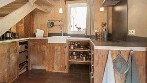 Una cocina rústica con vigas de madera, una ventana con cortinas y un colgador para ollas.