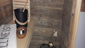 Una sala de sauna con un banco de madera, un cubo negro, un tazón de madera y un pequeño horno con una olla.
