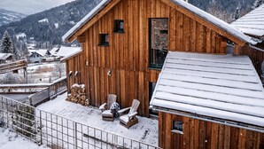 Una cabaña de madera con techo inclinado, una chimenea y un pequeño porche con dos sillas.