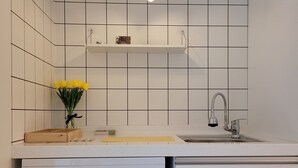 Cozinha com azulejos brancos, lava-louças, pia e luminária pendente.