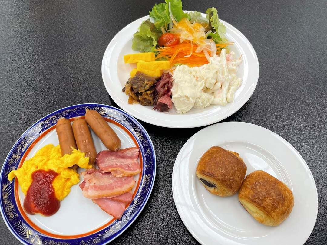 Drie borden eten: een met worst, eieren en bacon; een ander met salade en zuurkoolsalade; en een derde met gebak.