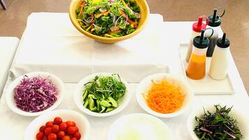 A table with various food items and condiments, including a bowl of salad, shredded vegetables, and small bowls of ingredients like tomatoes and cucumbers.
