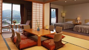 A traditional Japanese-style hotel room with tatami flooring, a low wooden table with cushions, a sliding shoji screen, and a balcony with a view of the mountains. - Hotel Tetora Resort Sendai Iwanuma (Iwanuma)