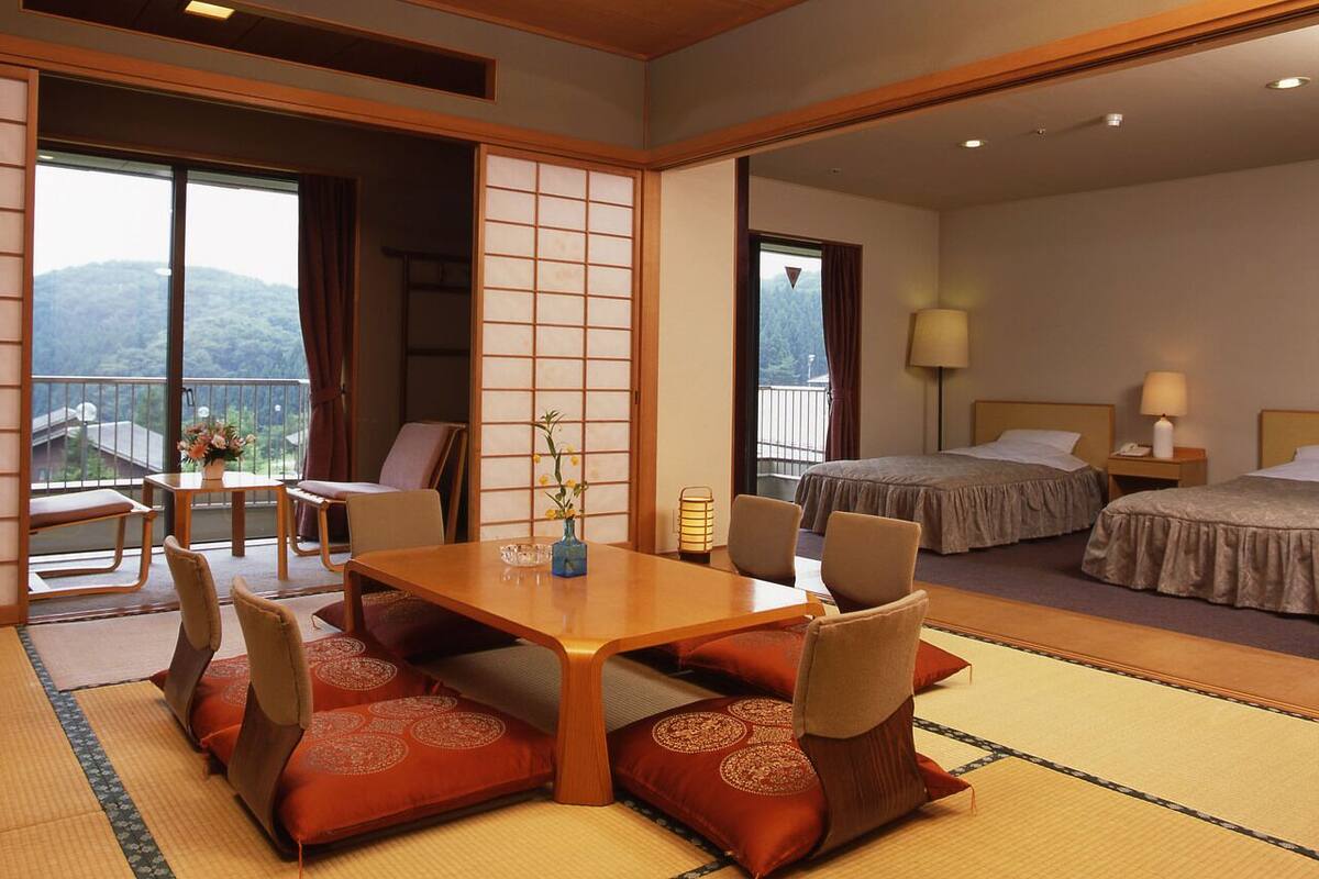 Et traditionelt japansk hotelværelse med tatamimåtter, et lavt træbord med hynder, en skydedør af shoji-papir og en balkon med udsigt til bjergene.