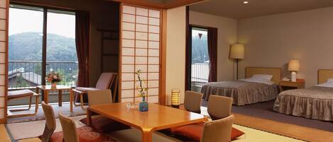 A traditional Japanese-style hotel room with tatami flooring, a low wooden table with cushions, a sliding shoji screen, and a balcony with a view of the mountains.
