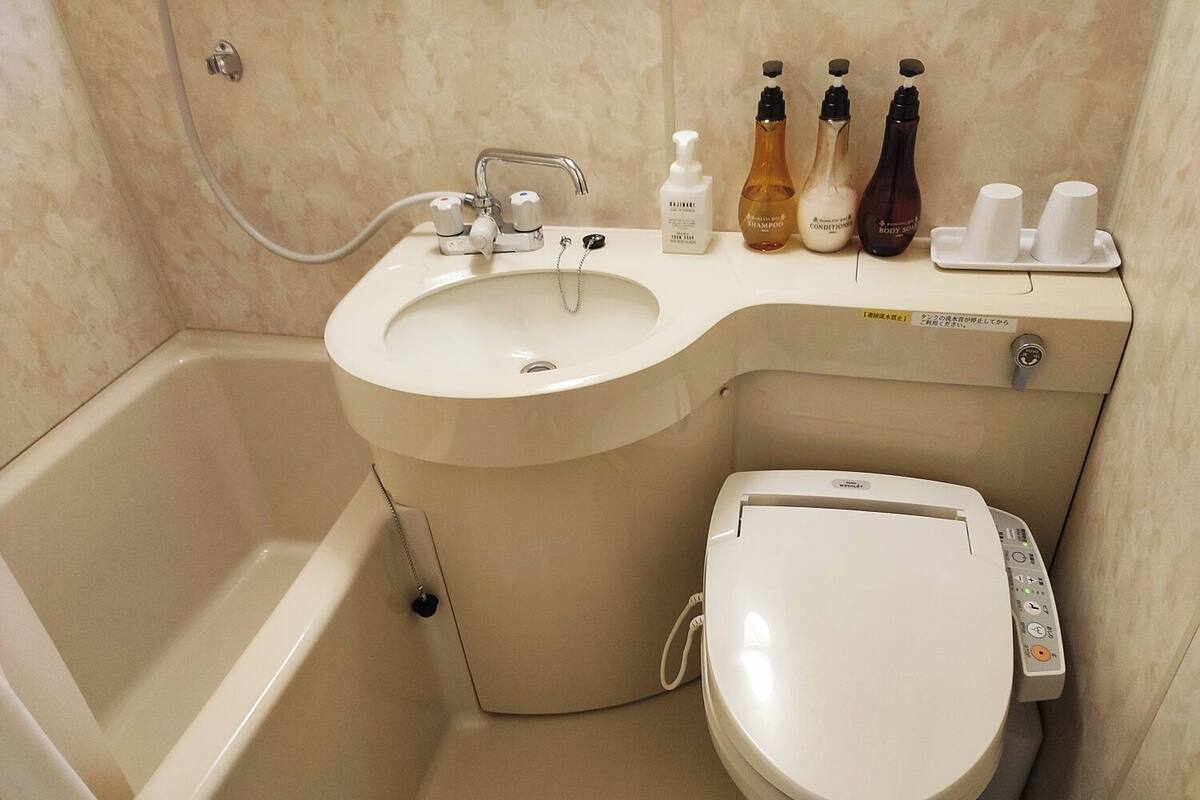Et badeværelse med badekar, toilet og håndvask. Der er toiletartikler på håndvasken.