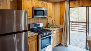 A kitchen with wooden cabinets, stainless steel appliances, a granite countertop, and a sliding glass door to a deck. - Studio style cabin in Twin Bridges with Mountain View’s near Sierra Ski Resorts (Twin Bridges)