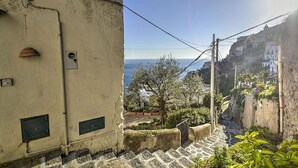 Una estrecha escalera conduce a una zona costera con vista al mar, un edificio de fachada desgastada y un árbol en primer plano.