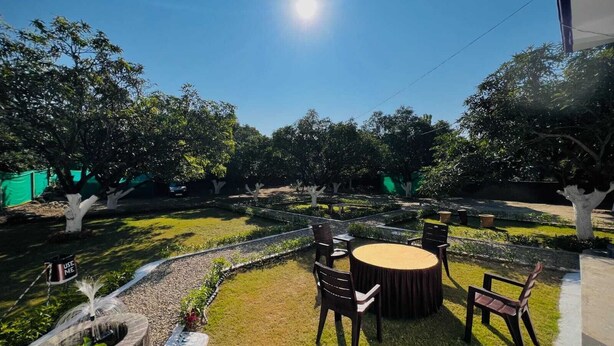 An outdoor seating area with a round table and chairs, surrounded by trees and a well-maintained lawn. - The Corbett Canopy Home Stay (Kaladhungi)