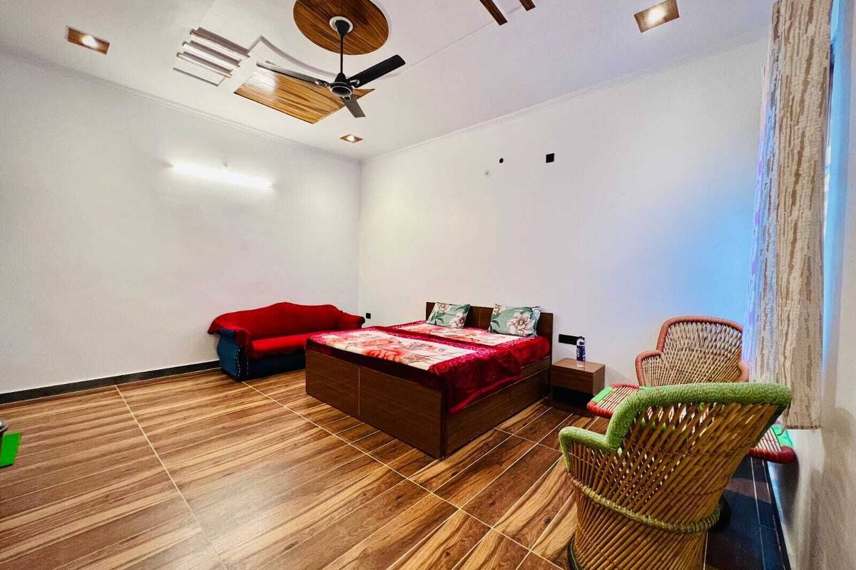 A bedroom with a bed, a red sofa, a wicker chair, and a ceiling fan.
