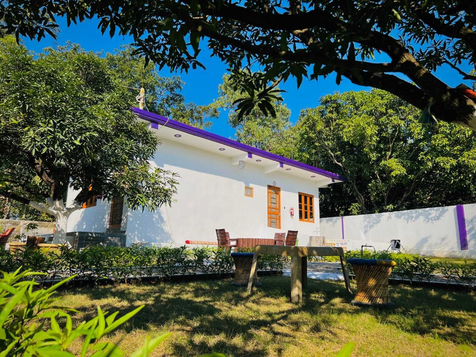 A white building with a purple roof, surrounded by lush greenery and trees.