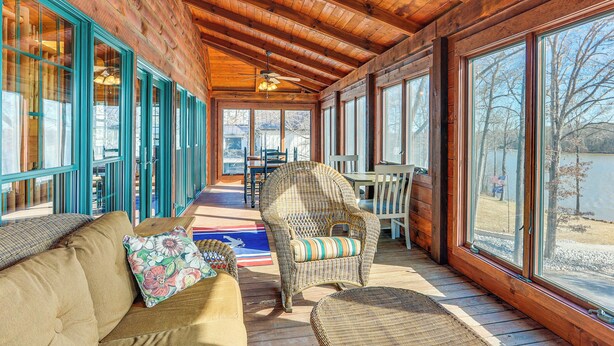 Une terrasse en bois avec un canapé et des fauteuils en osier, de grandes fenêtres et un ventilateur de plafond.
