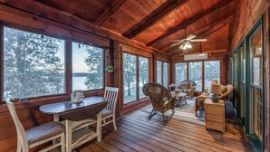 Une terrasse en bois avec une table et des chaises, des fauteuils à bascule en osier et un ventilateur de plafond.