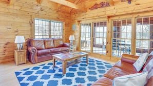 L’intérieur d’un chalet en bois, avec un canapé en cuir, une table basse et une grande fenêtre.