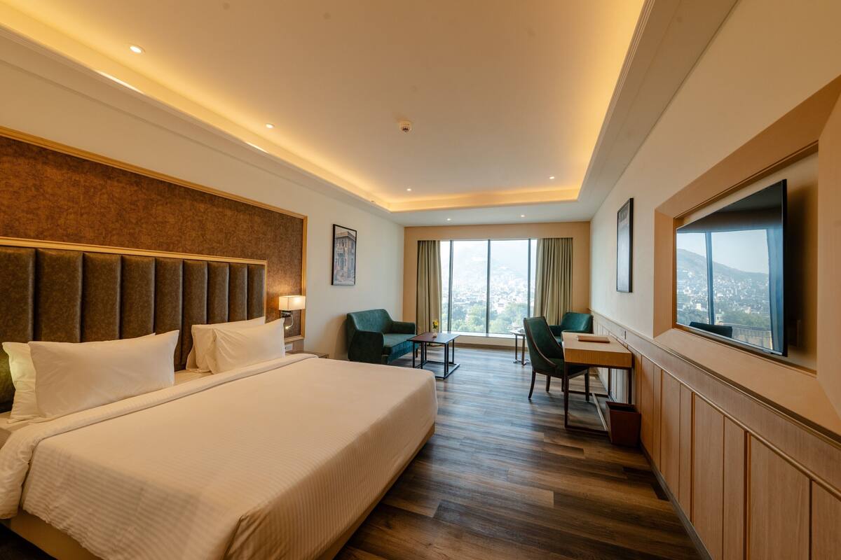 A hotel room with a large bed, a desk, a chair, and a TV.