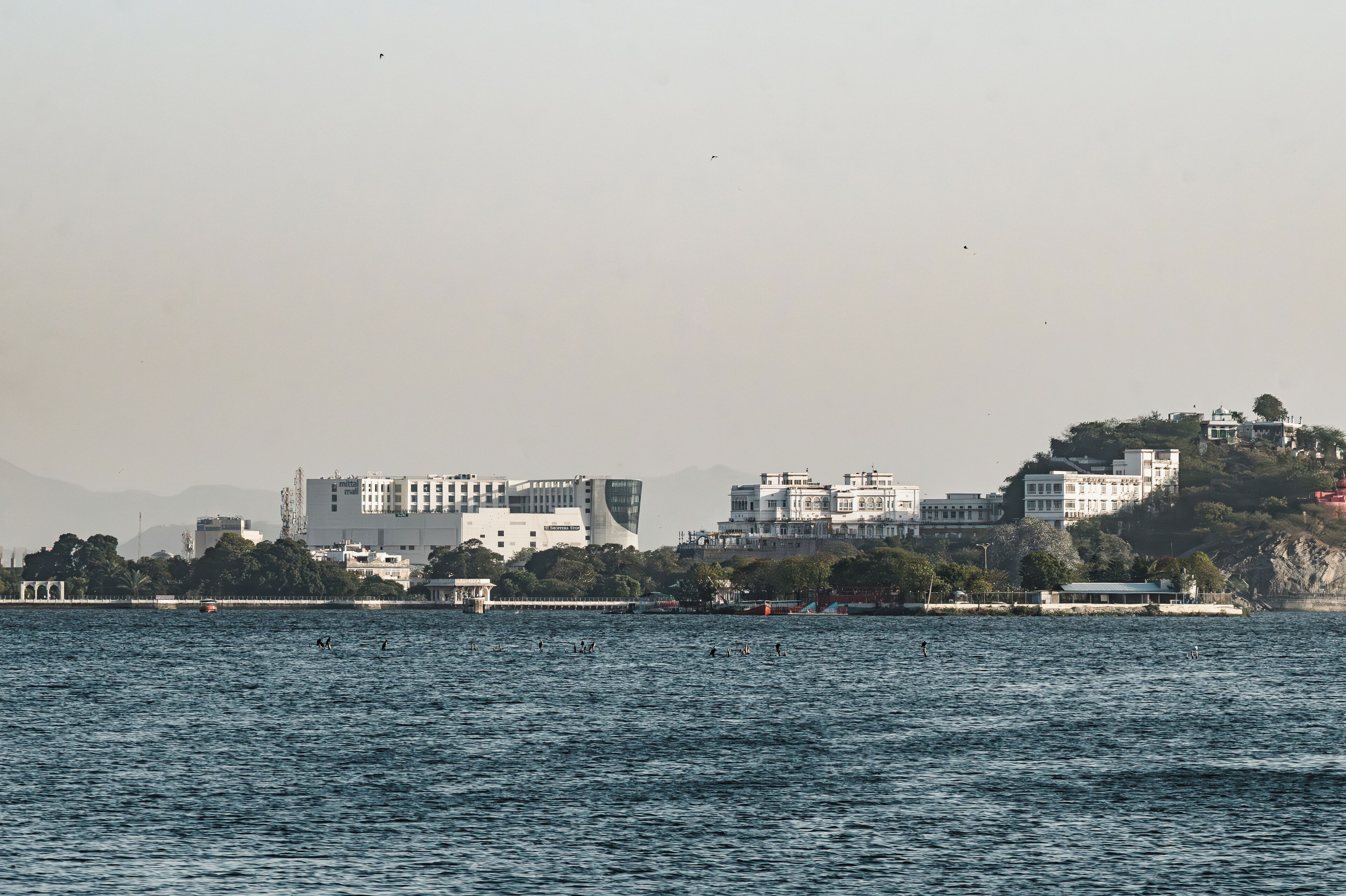 A waterfront view with buildings, including a prominent white structure with a curved facade and a sign that reads 'Shoppers Stop.'