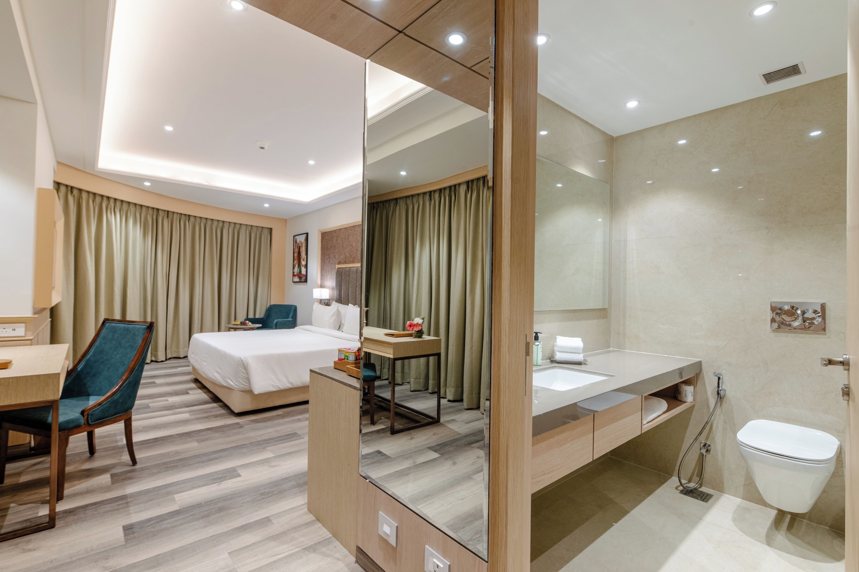 Habitación de hotel con cama, escritorio, silla y baño con lavamanos e inodoro.