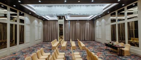 A conference room with rows of beige chairs, a patterned carpet, and a chandelier.