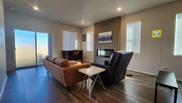 A spacious living room with a brown leather sofa, a black leather chair, a small white table, and a TV mounted on the wall. - Modern Salem Property (Salem)