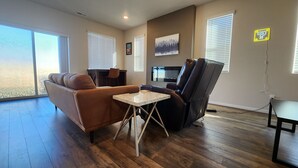 A living room with a brown sofa, a black leather chair, a small marble table, and a TV mounted on the wall. - Modern Salem Property (Salem)