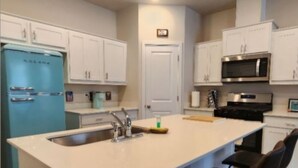 A modern kitchen with white cabinets, a blue refrigerator, a large island with a sink, and a microwave. - Modern Salem Property (Salem)