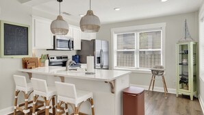 A modern kitchen with white cabinetry, a central island with bar stools, a microwave, and a refrigerator.