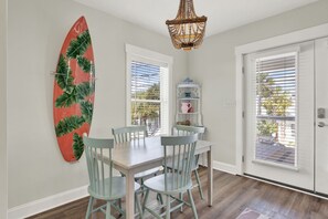 Een eethoek met een tafel en stoelen, een decoratief surfplank, een kroonluchter en uitzicht door het raam.