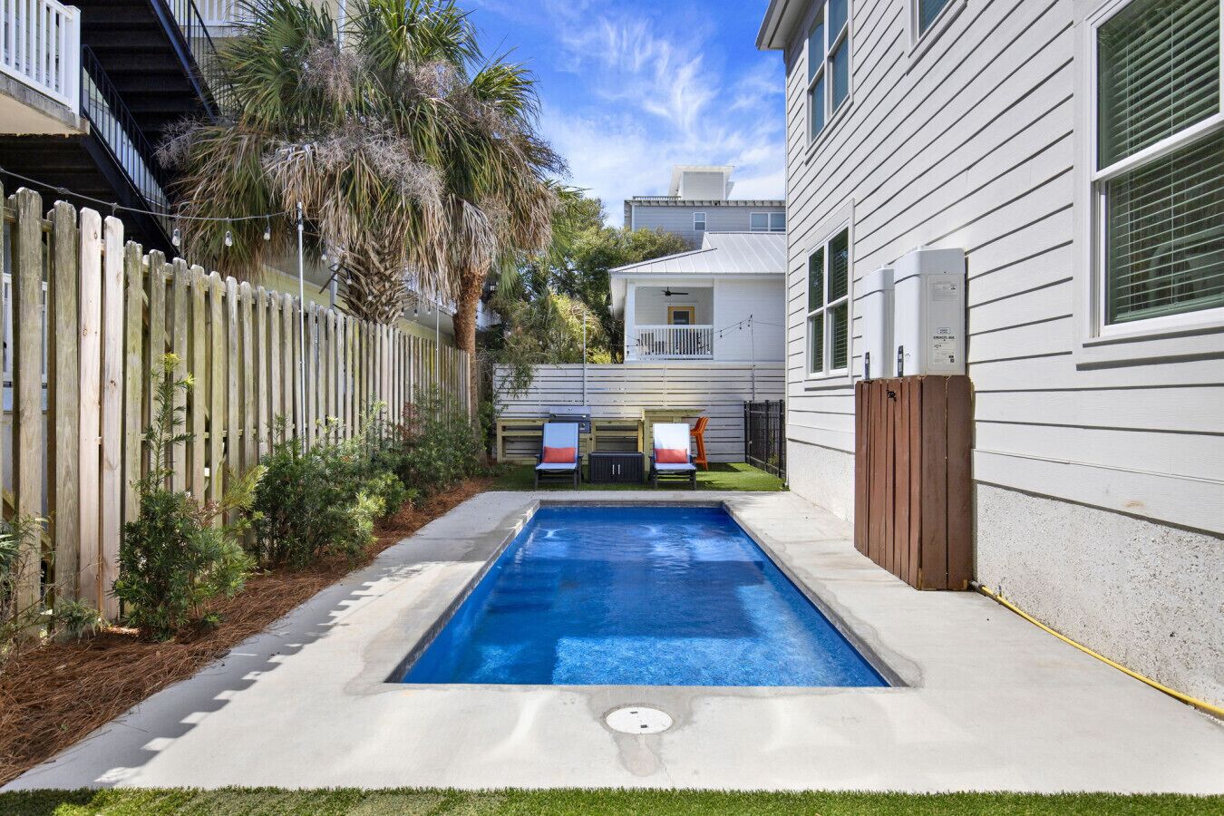 A swimming pool with a wooden deck, a fenced area, and a house with a garage.