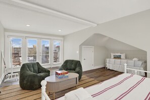 Een slaapkamer met schuine balken, een bed, een slaapbank, twee fauteuils, een klein tafeltje en een raam met zonwering.