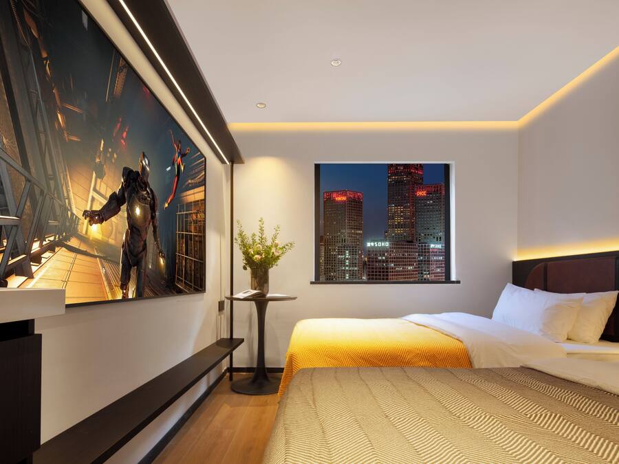Quarto de hotel moderno com uma cama grande, vista para a cidade, uma obra de arte emoldurada e uma pequena mesa com um vaso.