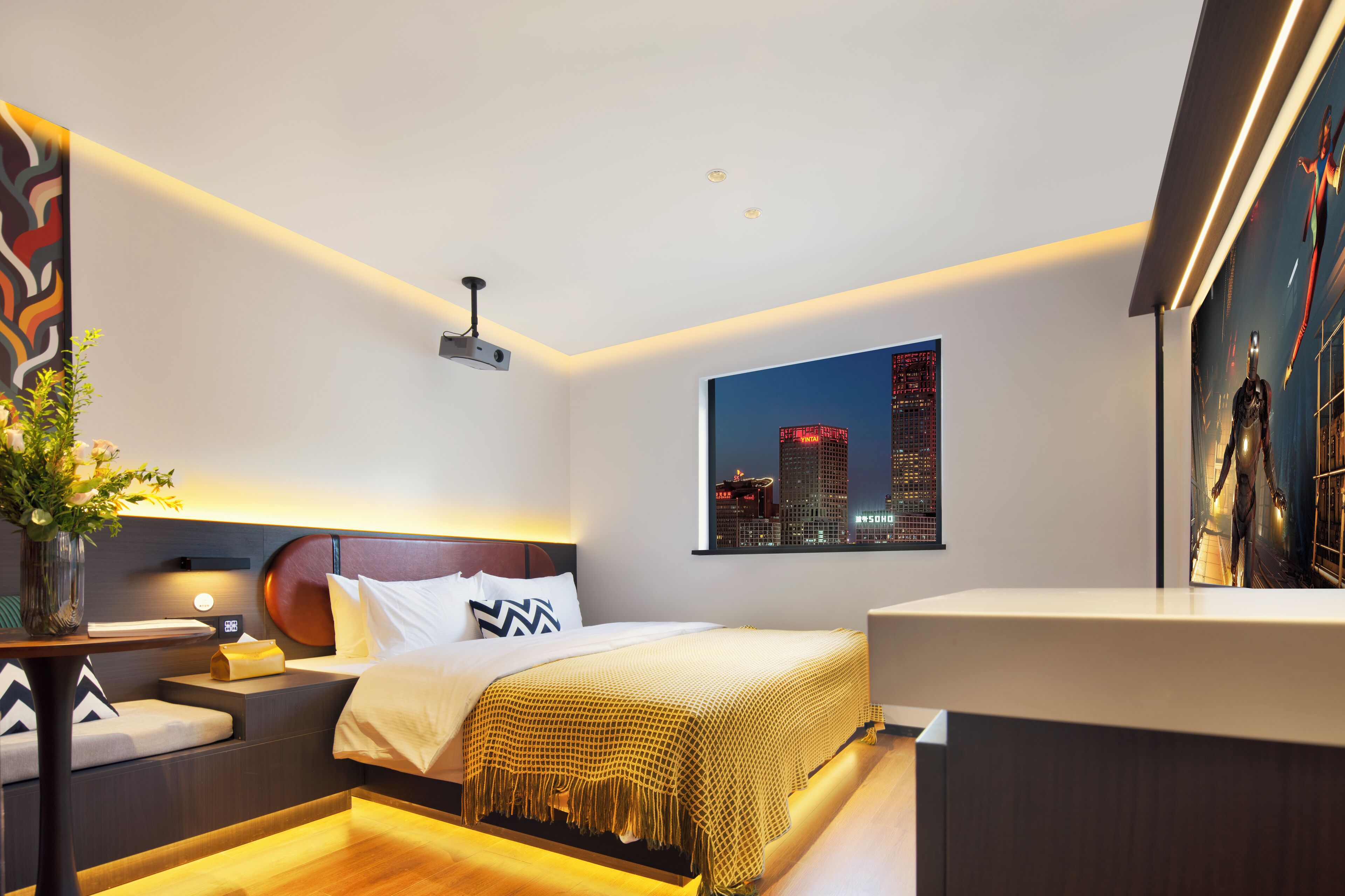 Une chambre d’hôtel moderne avec vue sur la ville, un lit agrémenté d’un couvre-lit à motifs, une table de chevet avec une lampe et une petite table de nuit ornée d’un vase de fleurs.