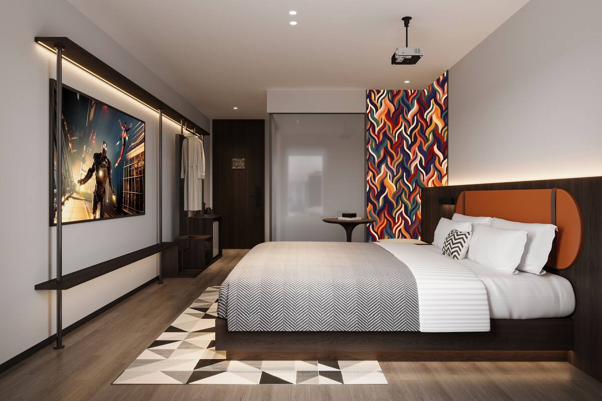A modern hotel room with a large bed, a mirror, a projector, and a colorful wall pattern.