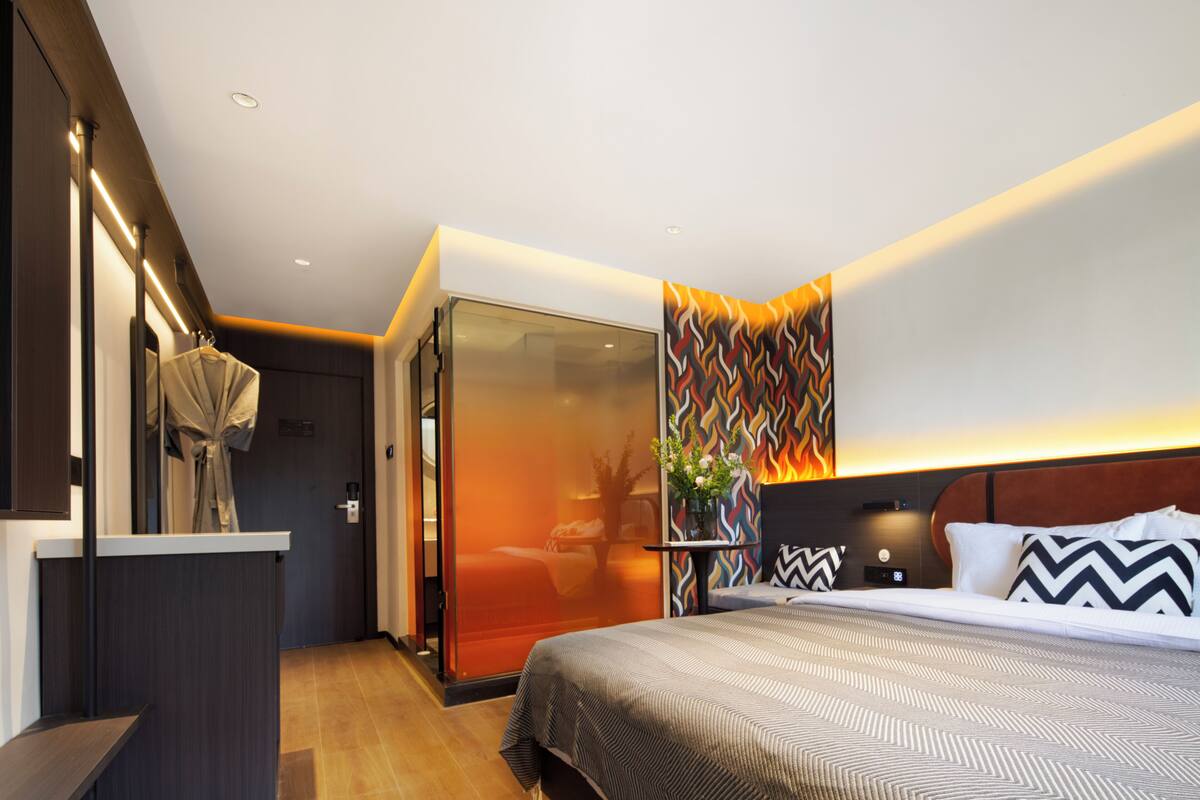 A modern hotel room with a large bed, a desk, and a glass partition.