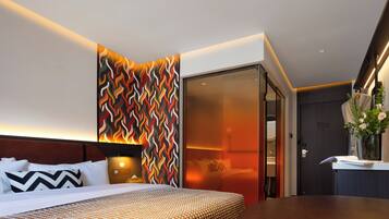 A modern hotel room with a bed, bedside table, and a wall with a colorful geometric pattern.