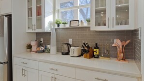 A kitchen with white cabinets, a coffee maker, a toaster, and various kitchen utensils. - The Cacti House - Hot Tub, Game Room, Cactus Mural, Minutes from Downtown Dallas (Dallas)