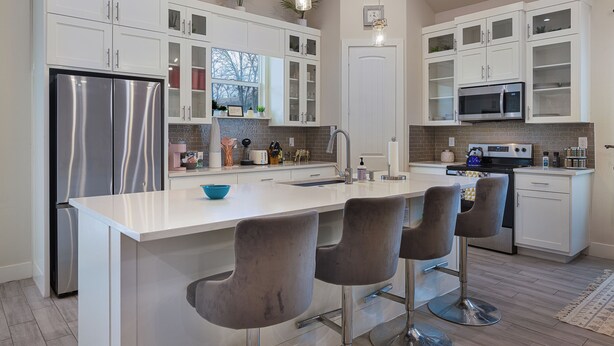 A modern kitchen with white cabinetry, a stainless steel refrigerator, a built-in microwave, and a large island with bar stools. - The Cacti House - Hot Tub, Game Room, Cactus Mural, Minutes from Downtown Dallas (Dallas)