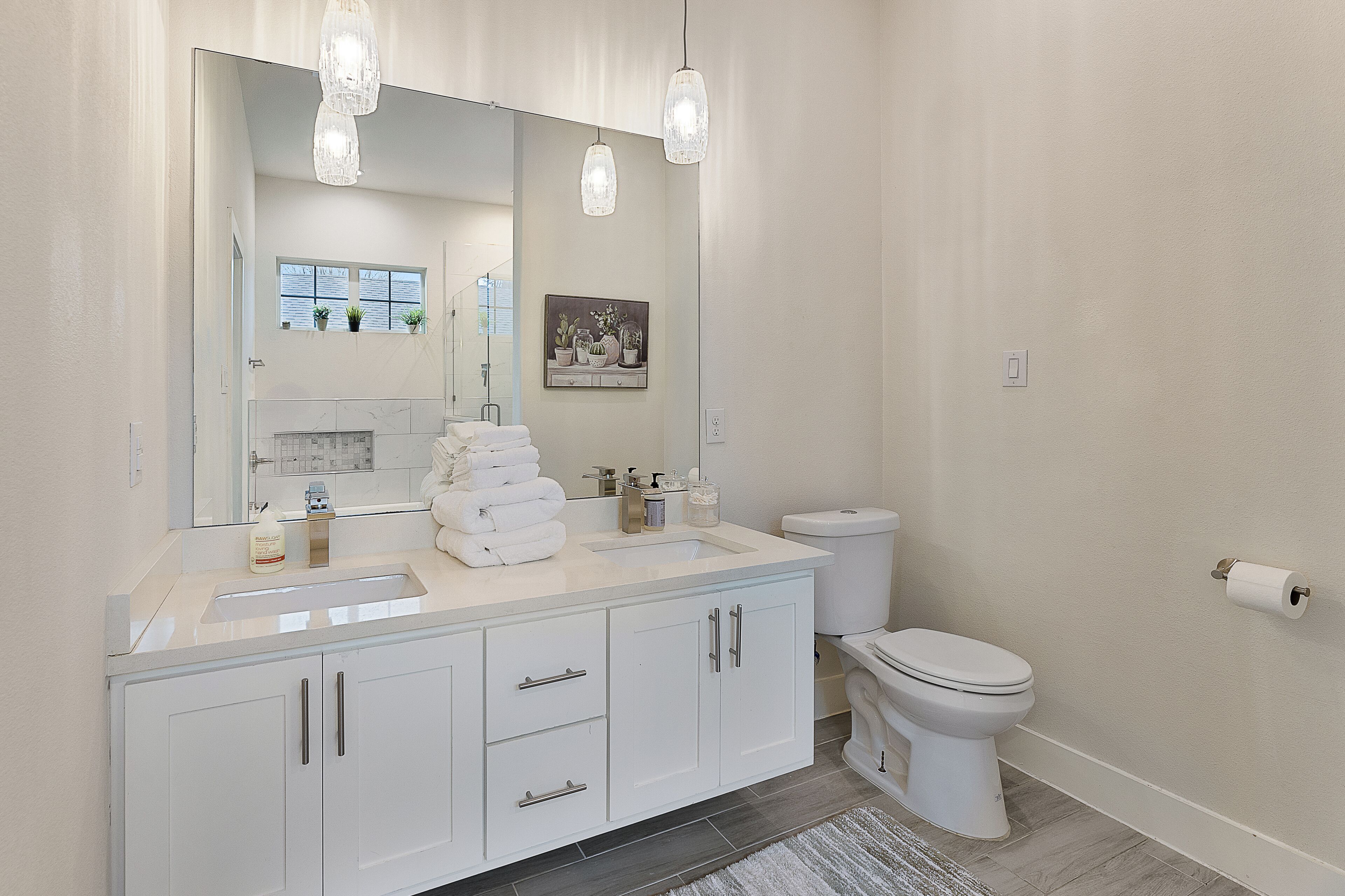 A modern bathroom with a large mirror, two pendant lights, a white toilet, and a sink with a marble countertop.