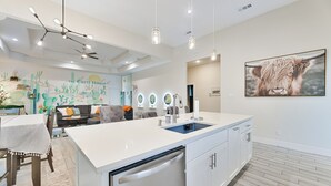 A modern kitchen with a white island, built-in dishwasher, and a large window. - The Cacti House - Hot Tub, Game Room, Cactus Mural, Minutes from Downtown Dallas (Dallas)