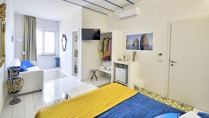 A hotel room with a bed, a sofa, a TV, a wardrobe, and a bathroom visible through an open door. - Appartamento Denise: A bright and cheerful apartment immersed in a splendid landscape, in the heart of a wonderful little town, with Free WI-FI. (Massa Lubrense)