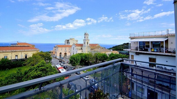 A coastal town with a prominent church, a road with vehicles, and a building with a balcony. - Appartamento Denise: A bright and cheerful apartment immersed in a splendid landscape, in the heart of a wonderful little town, with Free WI-FI. (Massa Lubrense)