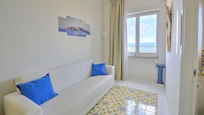 A white sofa with blue cushions, a patterned floor, a window with a view of the sea, and a decorative column. - Appartamento Denise: A bright and cheerful apartment immersed in a splendid landscape, in the heart of a wonderful little town, with Free WI-FI. (Massa Lubrense)
