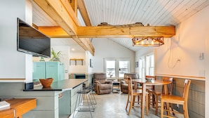 A modern kitchen with a dining area, wooden ceiling beams, and a built-in TV.