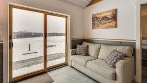 A cozy room with a sliding glass door leading to a snowy outdoor area, a beige sofa with patterned cushions, and a painting on the wall.