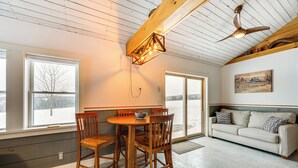 A spacious living area with a wooden dining table and chairs, a sofa, and a ceiling fan.