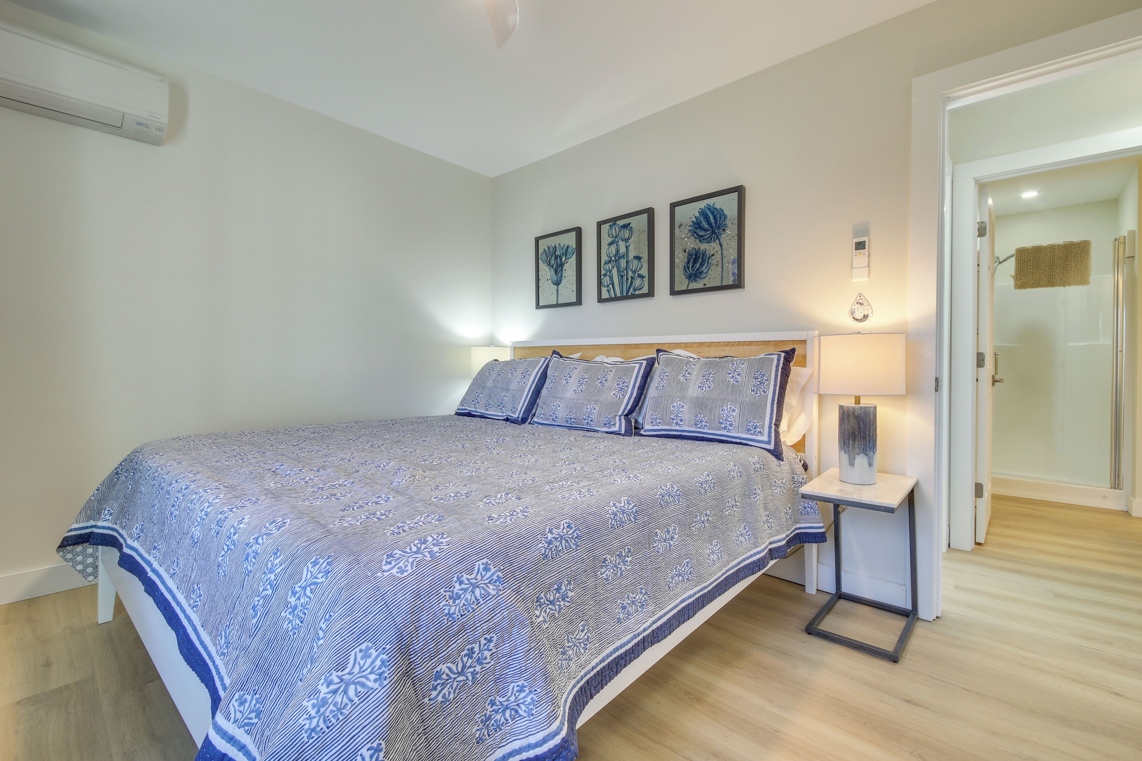 Une chambre à coucher avec un grand lit, une table de chevet avec une lampe et trois œuvres d’art florales encadrées accrochées au mur.