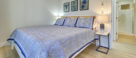 Une chambre à coucher avec un grand lit, une table de chevet avec une lampe et trois œuvres d’art florales encadrées accrochées au mur.