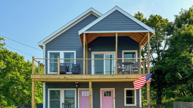 Ein zweistöckiges Haus mit Balkon, Veranda und einer Flagge.